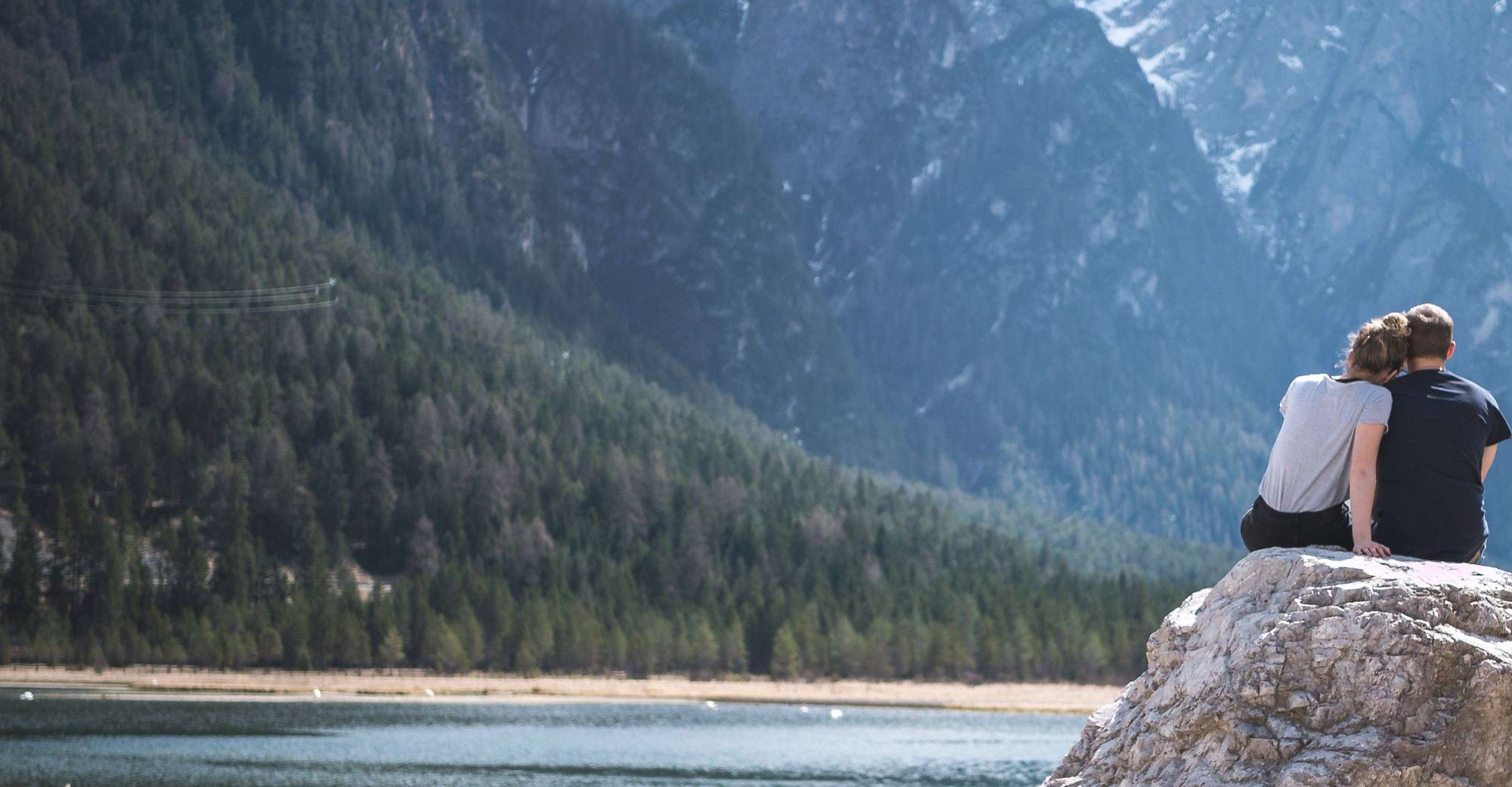 A couple sitting close together on a rock by a mountain lake